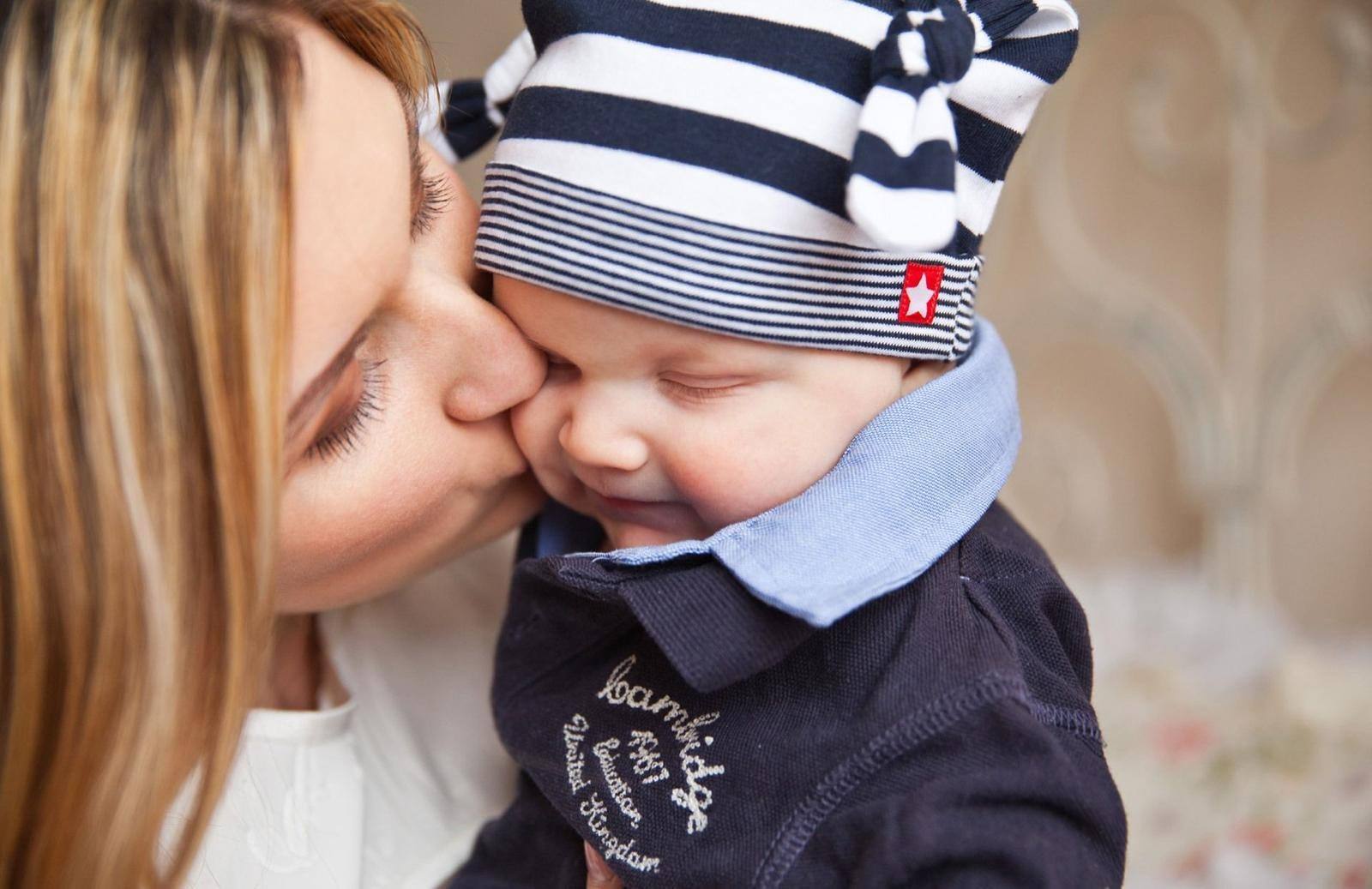 A carer giving a baby in a striped hat a kiss on the cheek
