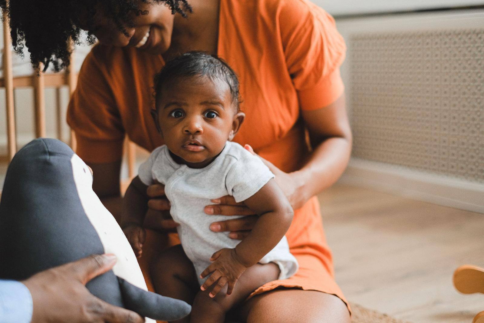 A baby sitting on a carer’s lap during play time at home