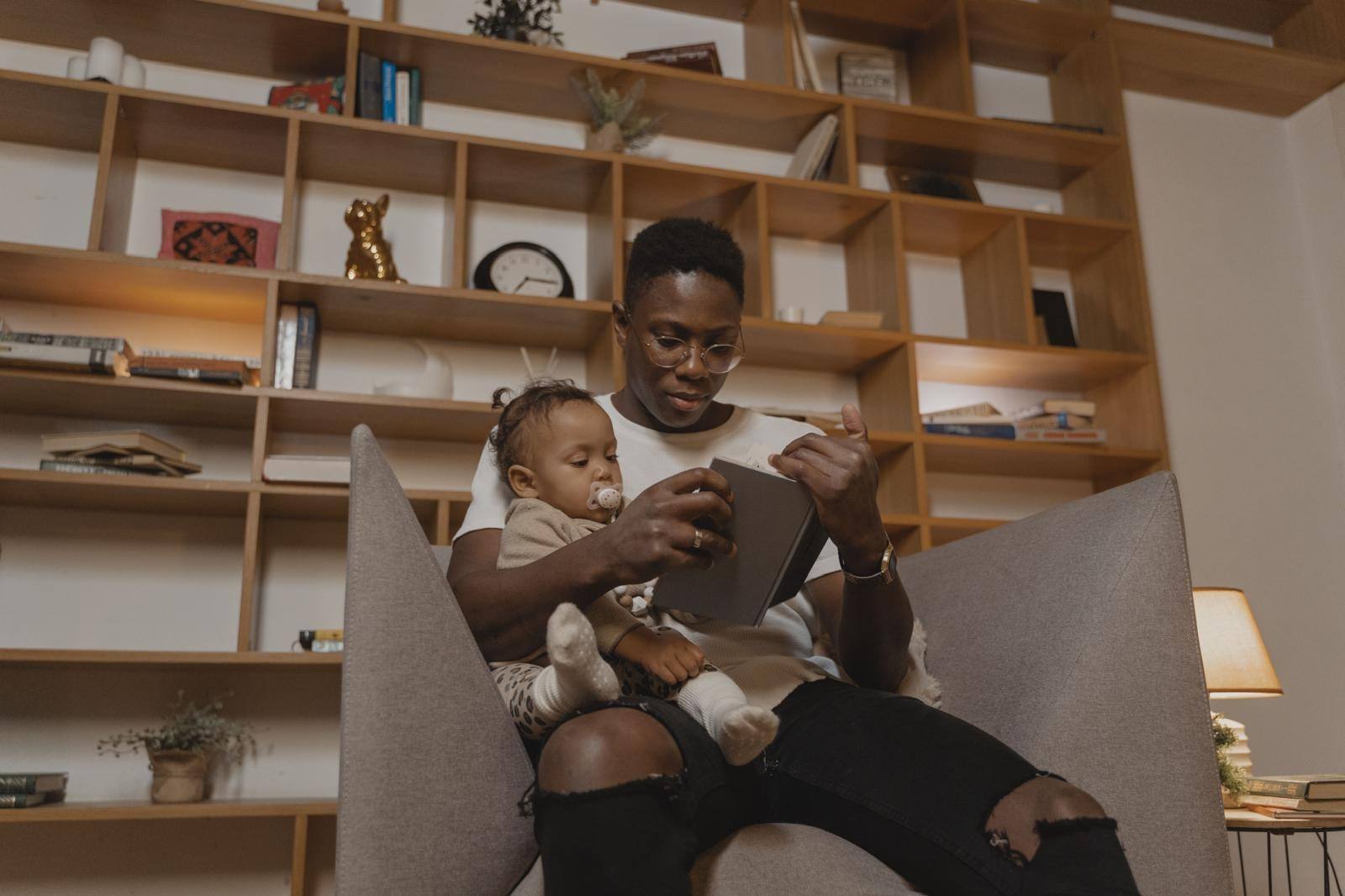 A carer reading a book with a baby on his lap in a living room armchair